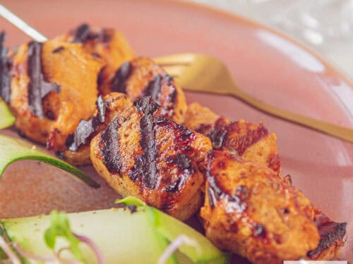 A square photo of two skewers on a red plate with chicken marinated in mustard and ketjap and grilled.