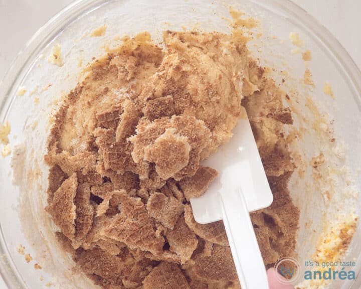 In a glass bowl, the stroopwafel is mixed into the batter with a white spatula.