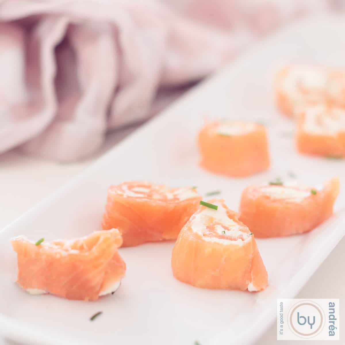 A square photo showing part of a long tray of salmon rolls filled with cream cheese and chives