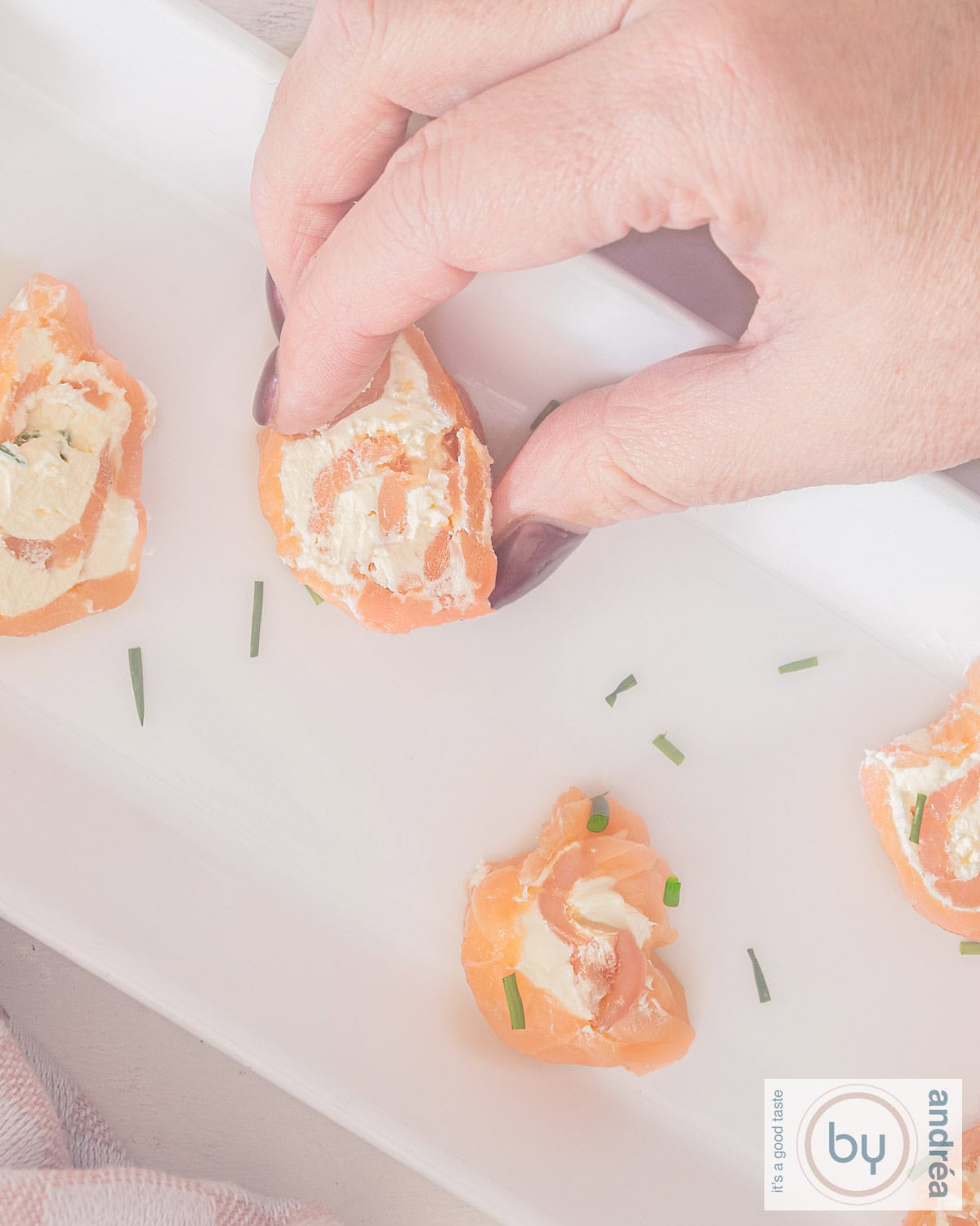 A picture from above with salmon cream cheese rolls. A hand taking a finger food.
