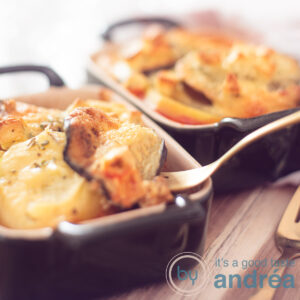 A square photo with two individual oven dishes filled with Greek moussaka on a wooden board
