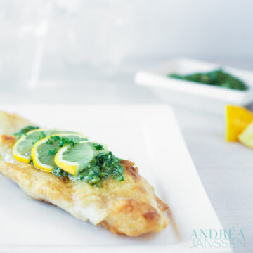 a white plate with pangasiusfilet filet with arugula pesto and slice of lemon