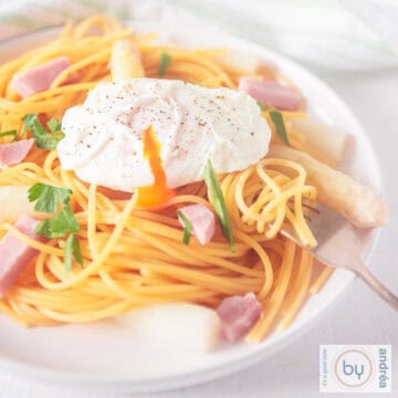 A square picture of a white plate with spaghetti, ham asparagus and poached egg.