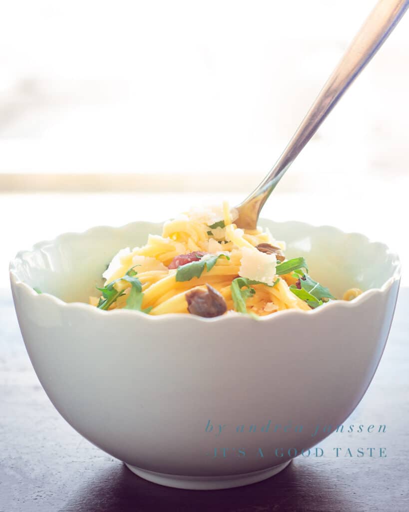 a white bowl with spaghetti, arugula and capers
