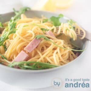 A square photo net a gray bowl filled with ham, arugula and spaghetti on a white background