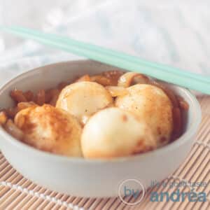 A square photo with a gray dish filled with Bali bumbu from Eggs. Two blue chopsticks lie on it. A white blue towel in the background.