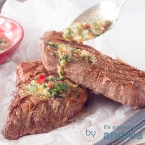 a square photo with white bakign paper where two grilled steaks are on top. a spoon adds some chimichurri sauce