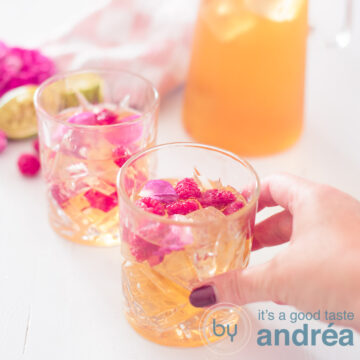 A square picture with lime rose and raspberry iced tea, two glasses and a jar diagonally. A hand is taking the first glass.