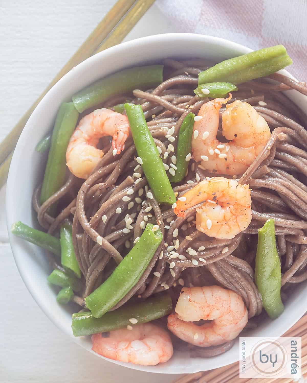 Een foto van bovenaf van een wit schaaltje met garnalen, boontjes, sesamzaad en noedels