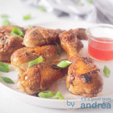 A square photo of a white plate with five drumsticks with spring onion and chilli sauce