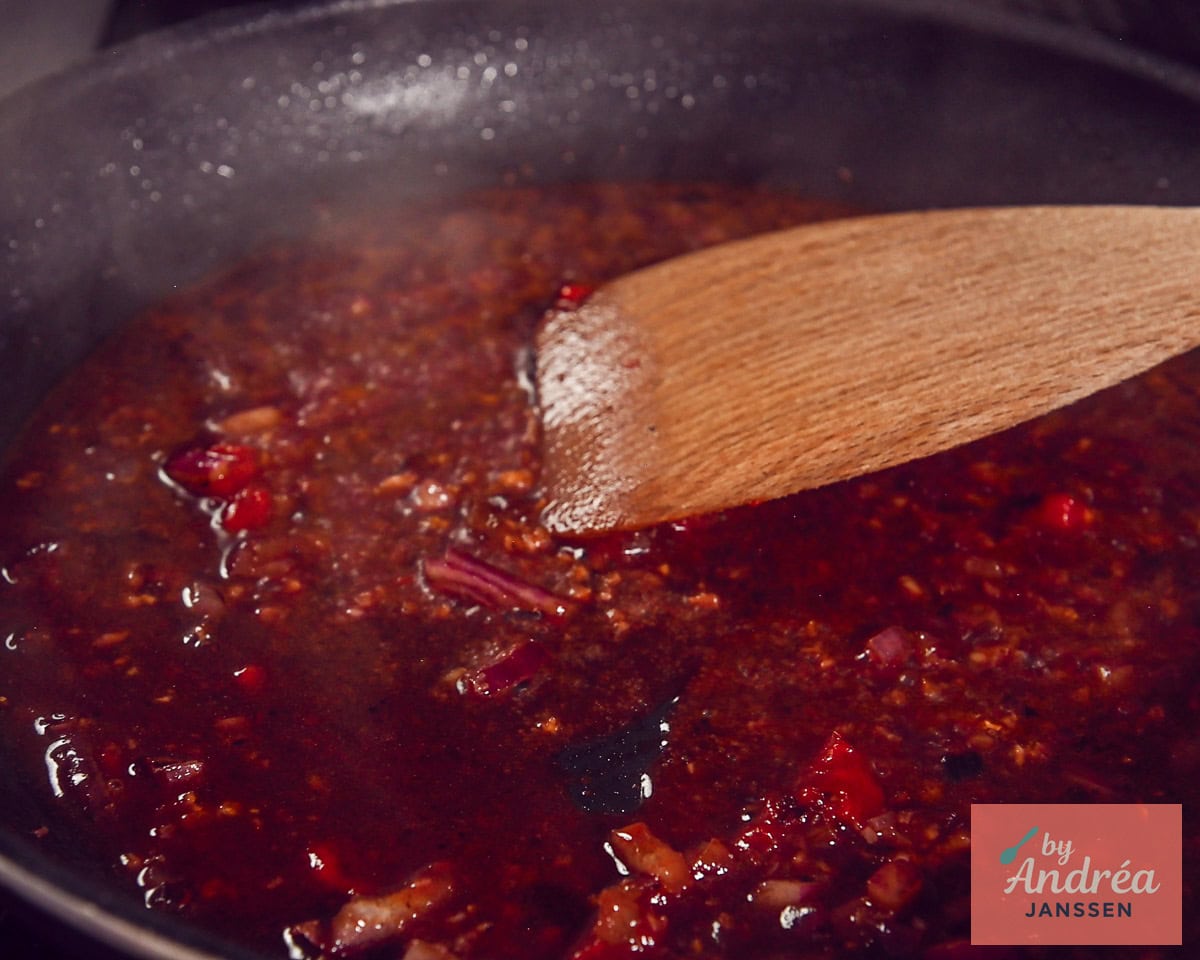 Pizzaiola sauce with pieces of red onion is stirred in a skillet with a wooden spatula.