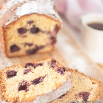 A wooden board with a cake with blueberries. Two slices off. A cup of coffee on the right