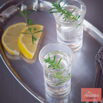 A square photo with a silver tray with two glasses of ouzo, lemon and rosemary.