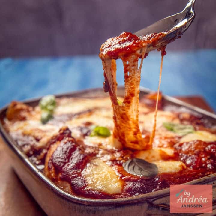 Chicken pizzaiola with tomato sauce and stretchy mozzarella is lifted from the baking dish with a fork.