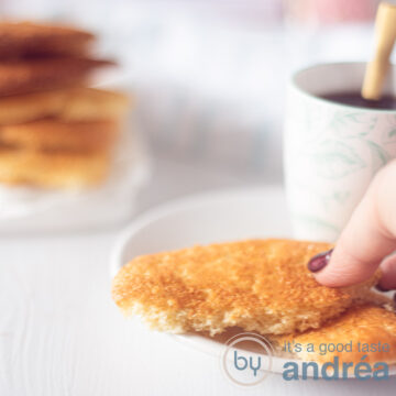 A white background with a white plate with two half egg cakes on the right side. A hand takes an egg cake. In the back left a stack of egg cakes.