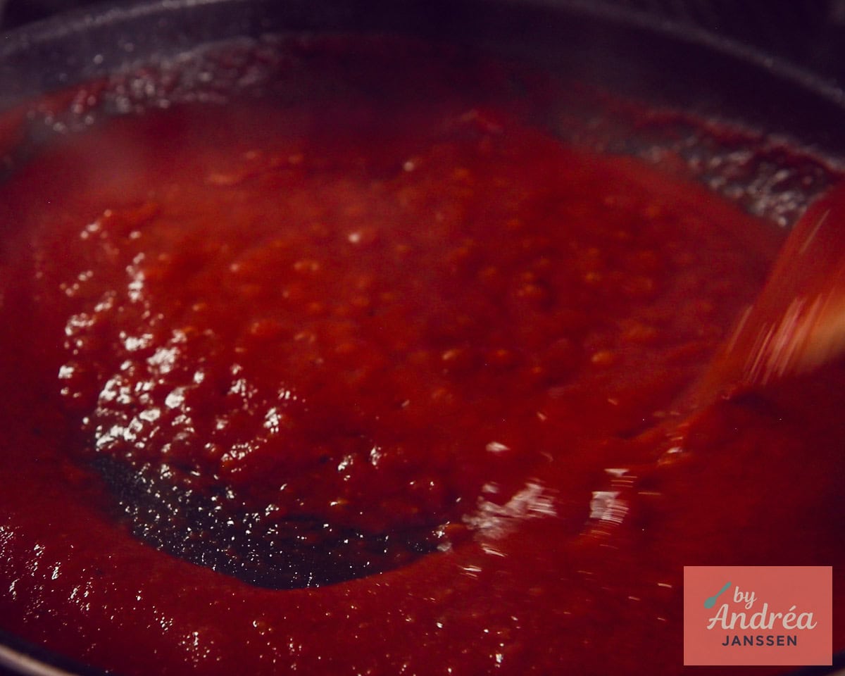 Thick tomato sauce for chicken pizzaiola is stirred in a skillet.