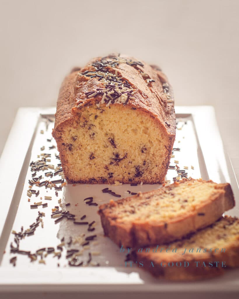 Een halve hagelslag cake op een wit bord, enkele plakjes en hagelslag eromheen gestrooid