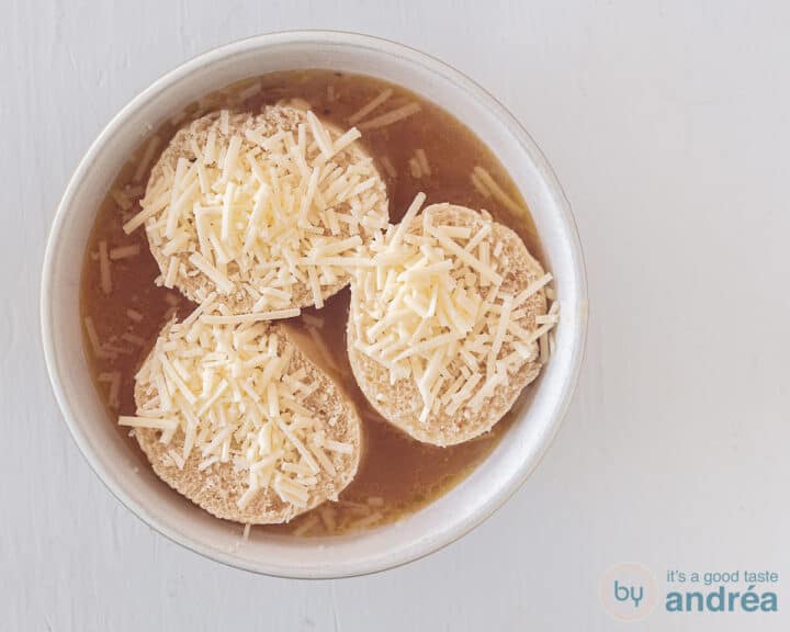 Onion soup in a white bowl. Inside are three slices of baguette with grated cheese.