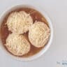 Onion soup in a white bowl. Inside are three slices of baguette with grated cheese.