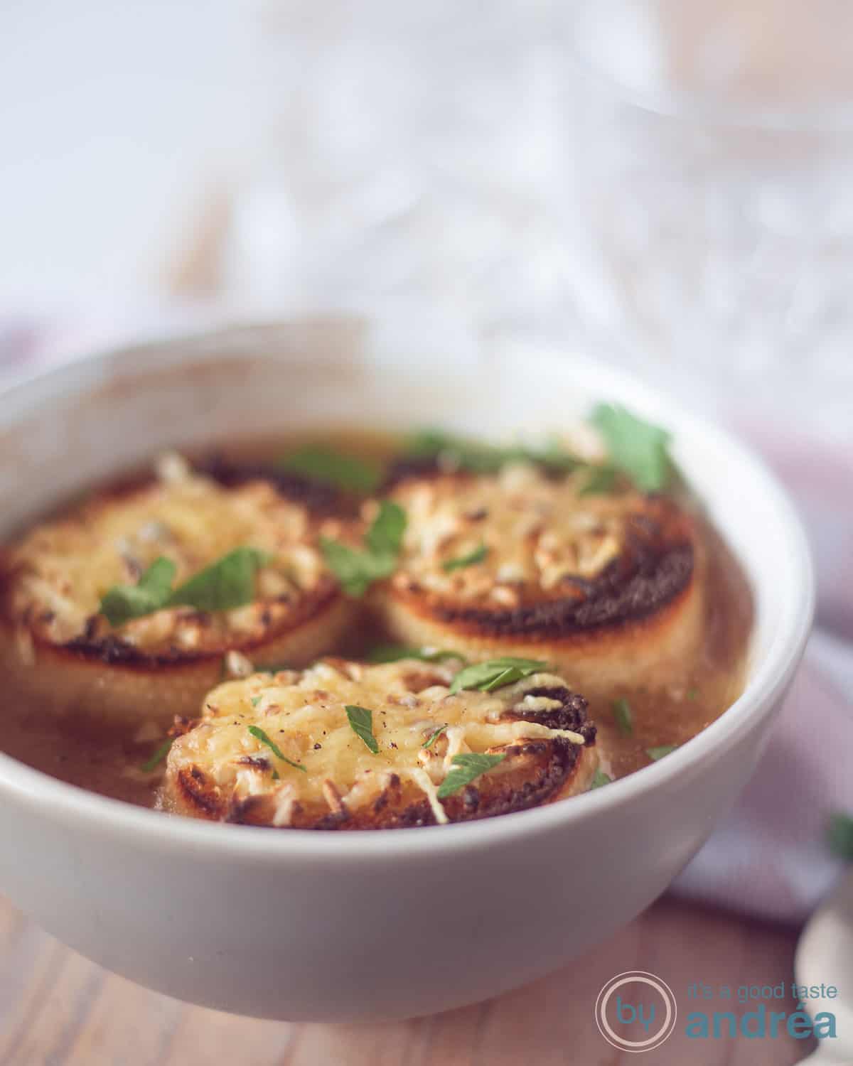 Een hoogtefoto van een grijze kom met bier uiensoep met daarop drie stokbroodjes drijvend met gegratineerde kaas. Op een houten plank.