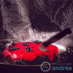 A square picture of a chocolate Halloween cake with a red cream cheese topping. Decorated with insects and knifes. A dark background