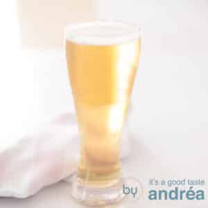 A square photo with a beer cocktail of lager and apple cider on a white surface. A pink white tea towel behind it.