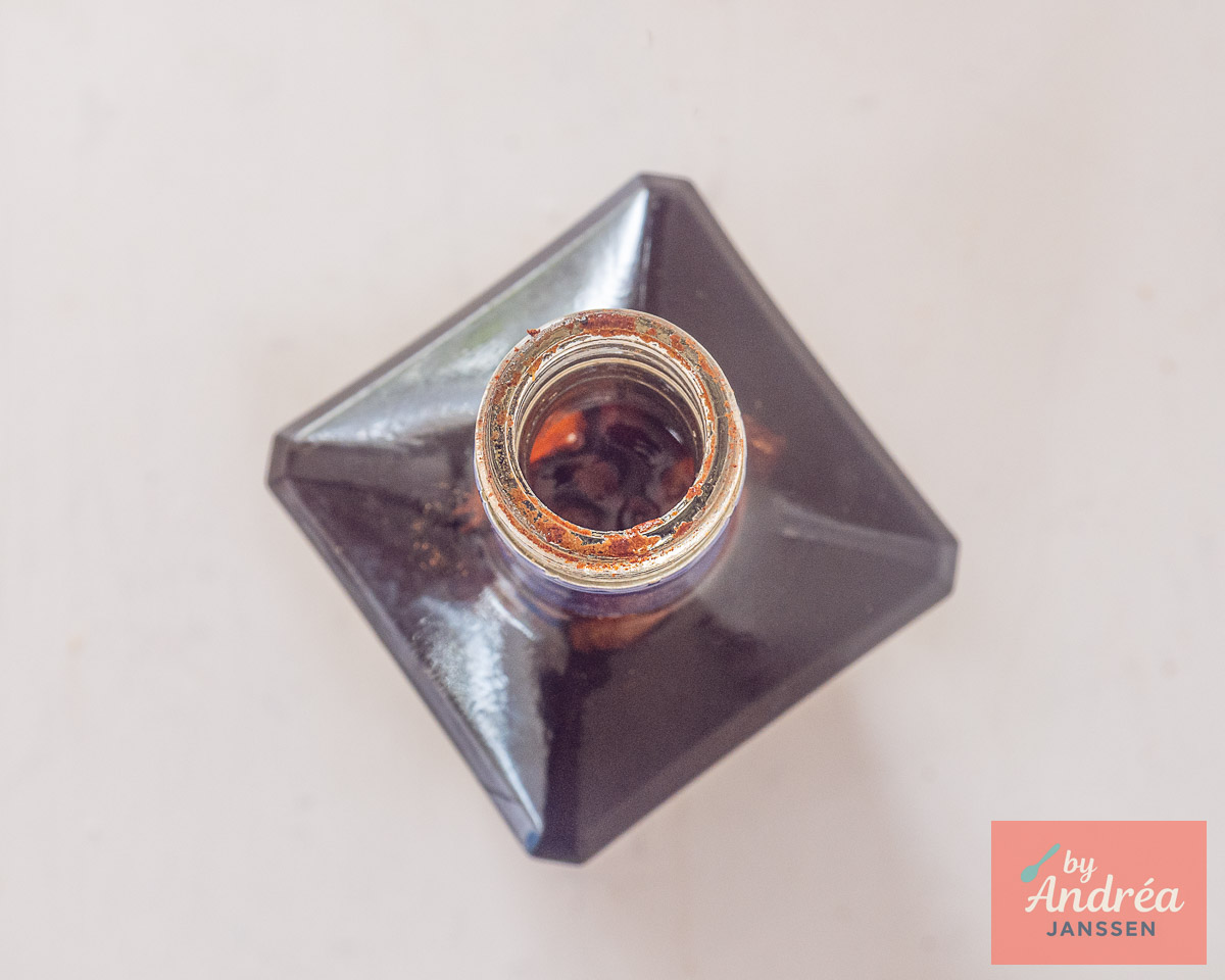 Overhead view of an open bottle filled with dark spiced liqueur and whole spices