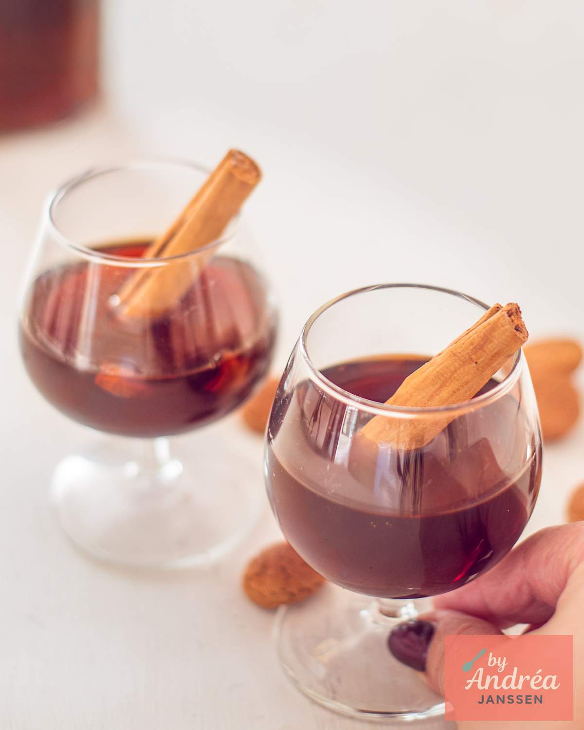 Hand holding a glass of homemade spiced liqueur with a cinnamon stick