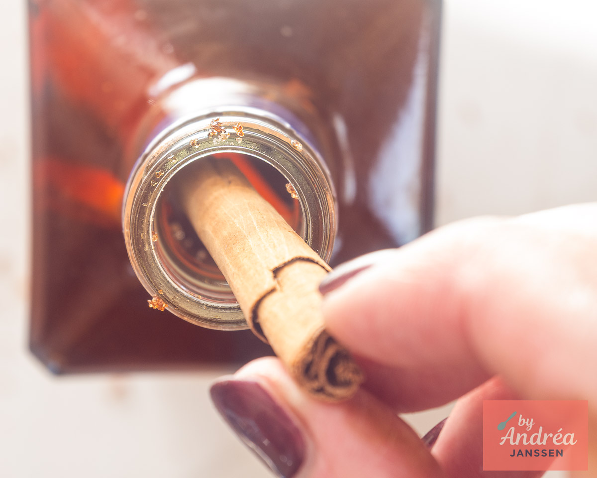 A cinnamon stick being placed inside a bottle of homemade spiced liqueur