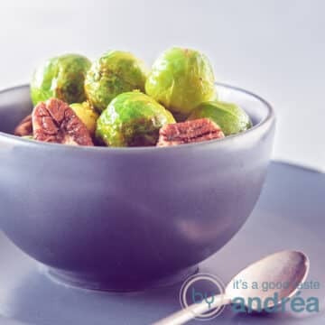 A square photo with a gray bowl filled with Brussels sprouts, pecan and delicious orange glaze. A dark gray background. A spoon in the front.