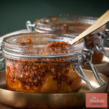 Close-up of apple pieces beneath a baked oat crumble topping in a clamp-top jar, with a second jar in the background.