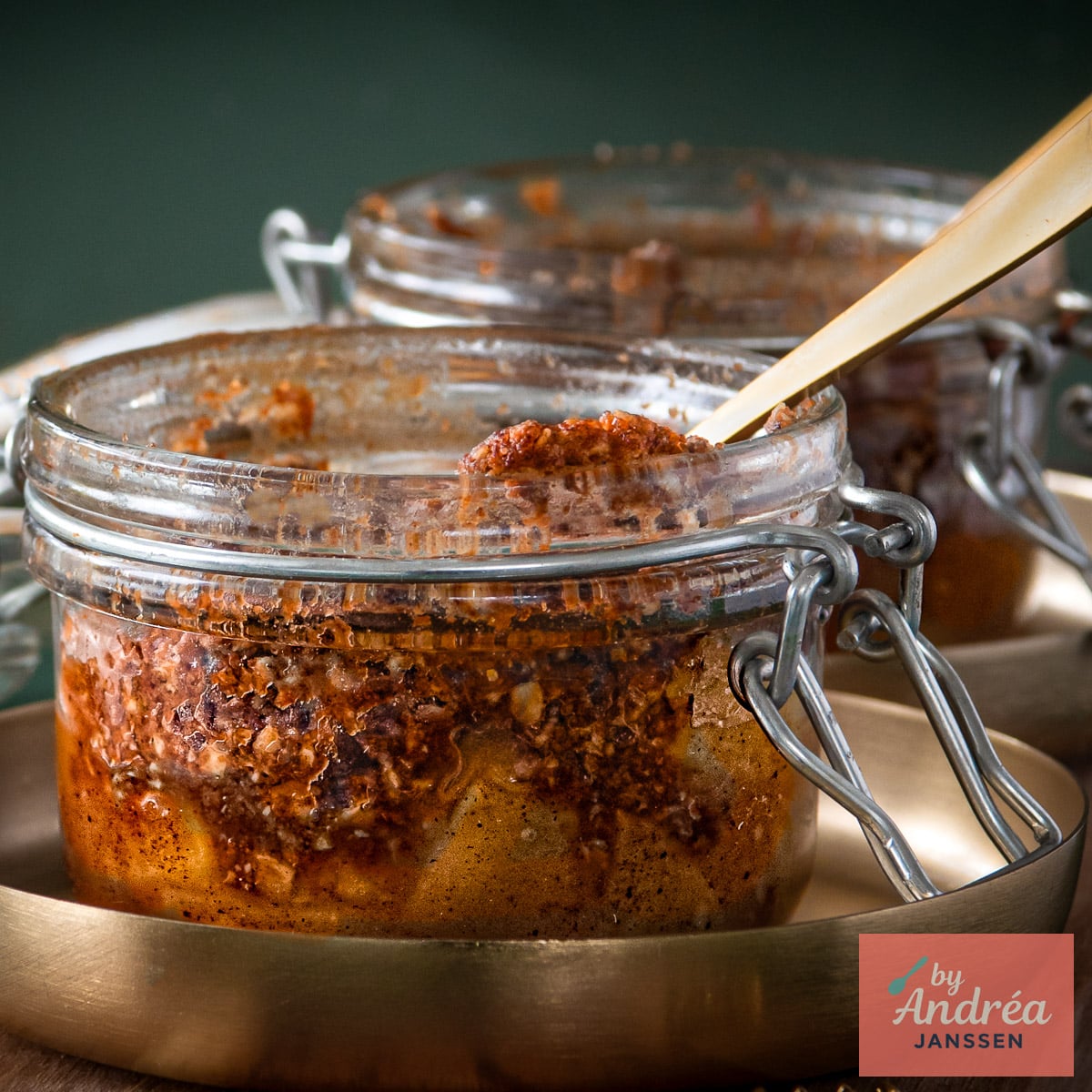 Close-up of apple pieces beneath a baked oat crumble topping in a clamp-top jar, with a second jar in the background.
