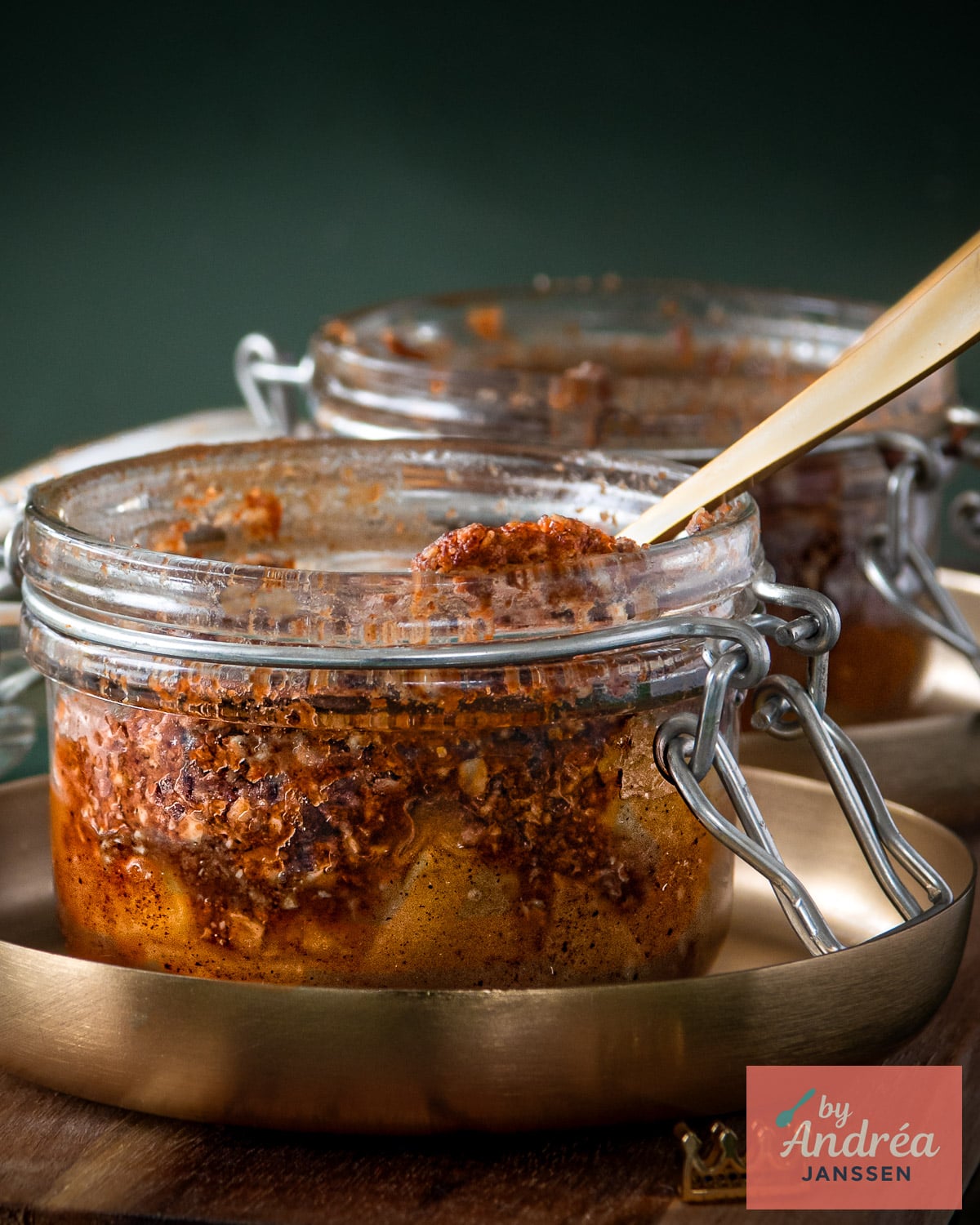 Apple crumble with a browned oat topping in a clamp-top glass jar with a gold spoon on a serving tray.