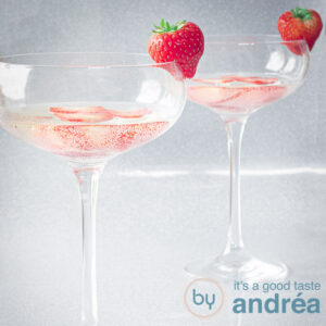 a square photo of two champagne glasses filled with Prosseco and fresh strawberries on a silver background