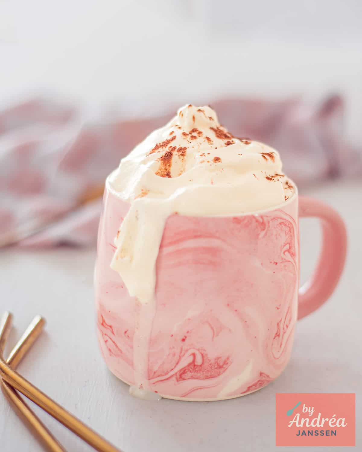 A pink cup filled with hot chocolate and baileys topped with whipped cream.