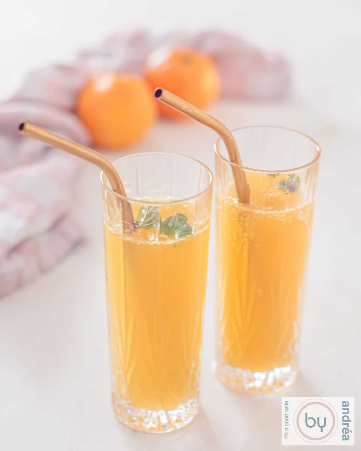 Een hoogtefoto met twee glazen gevuld met mandarijn champagne cocktail met gouden rietjes.