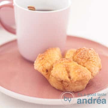A square photo of a pink plate with a cup of coffee and a monkey bread muffin in front of it.