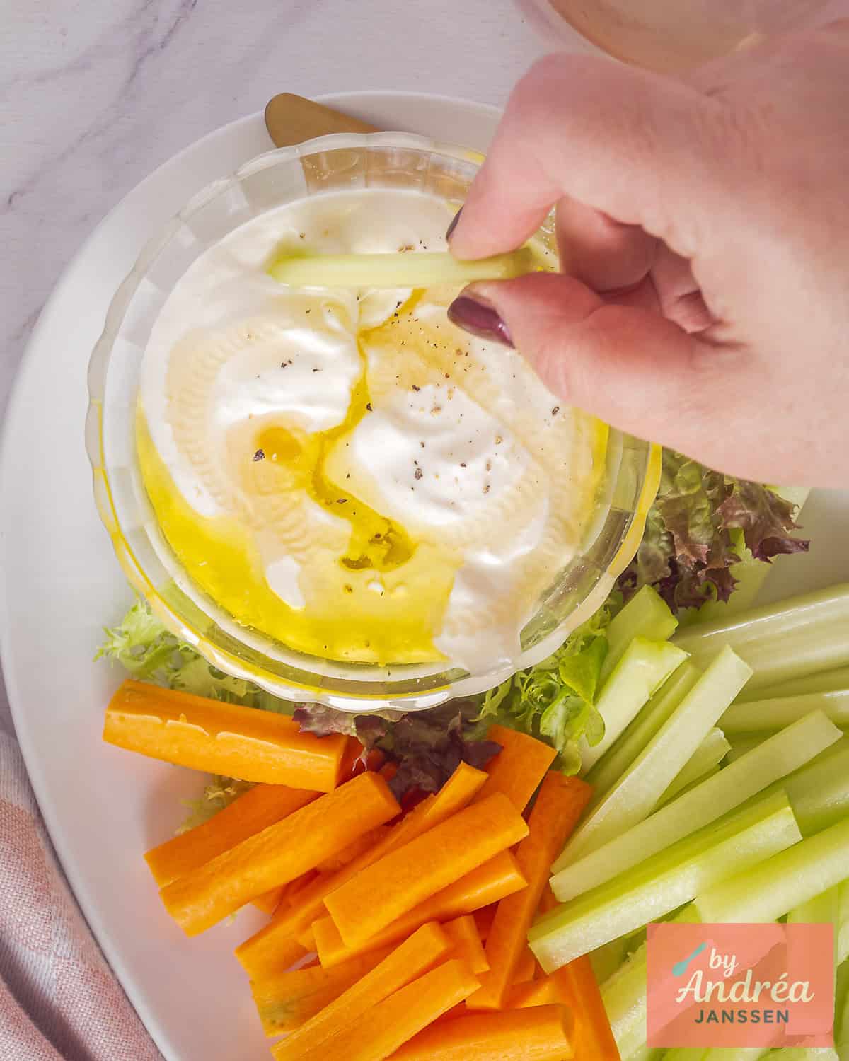 Een foto van bovenaf van whipped feta dip met olijfolie. En groenten eromheen. Een hand dipt groente in de dip.