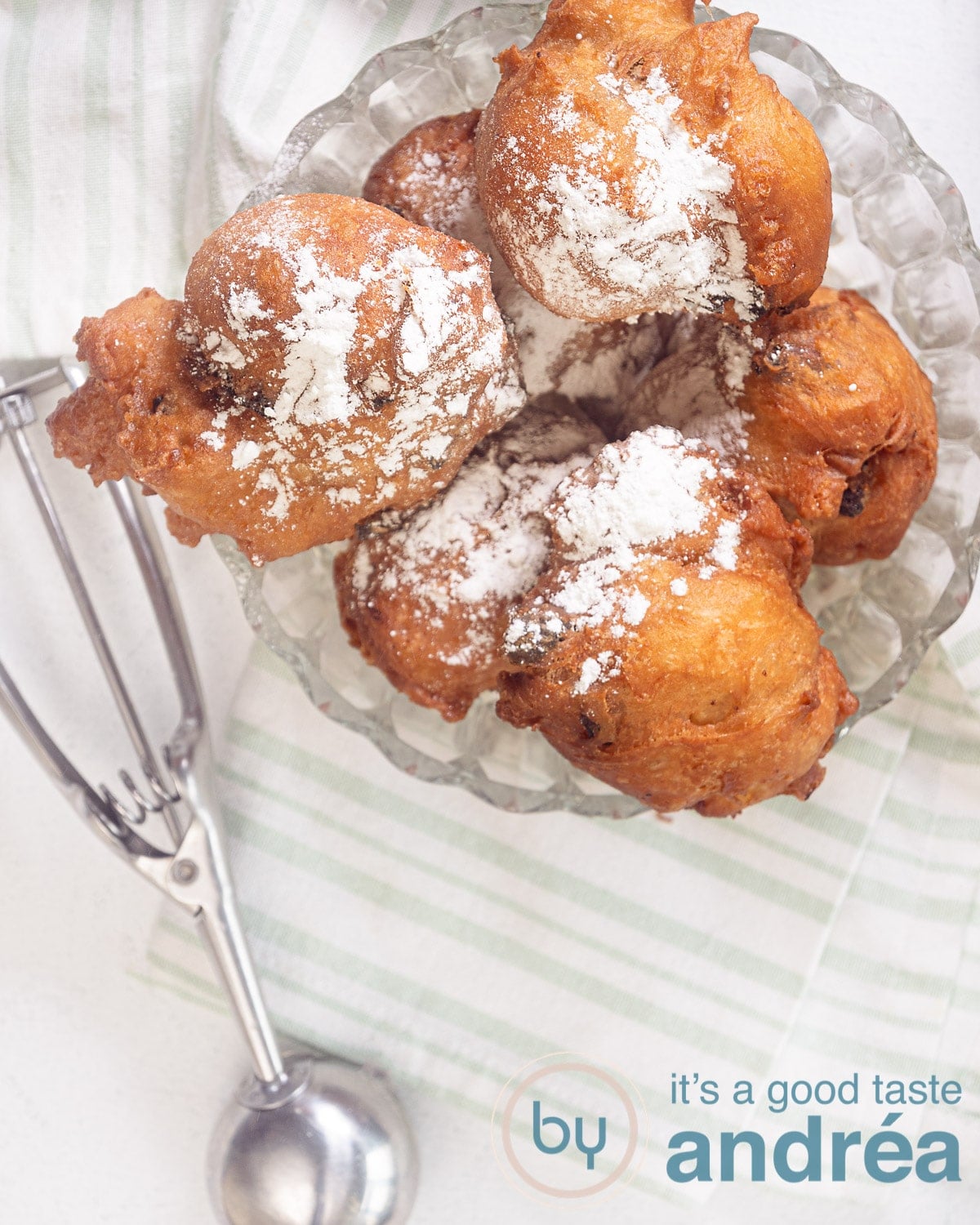 a top photo of a glass bowl filled with oliebollen. An ice cream scoop at the bottom