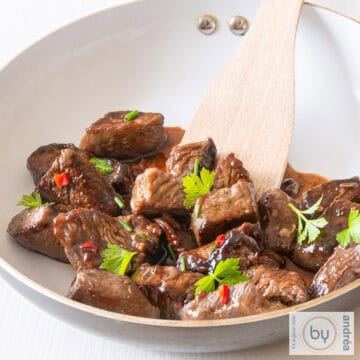 A square photo with a white pan with steak tips, pepper and coriander.