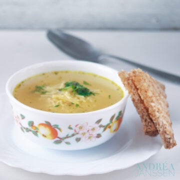 a bowl with noodle soup with herbs and a slice of bread