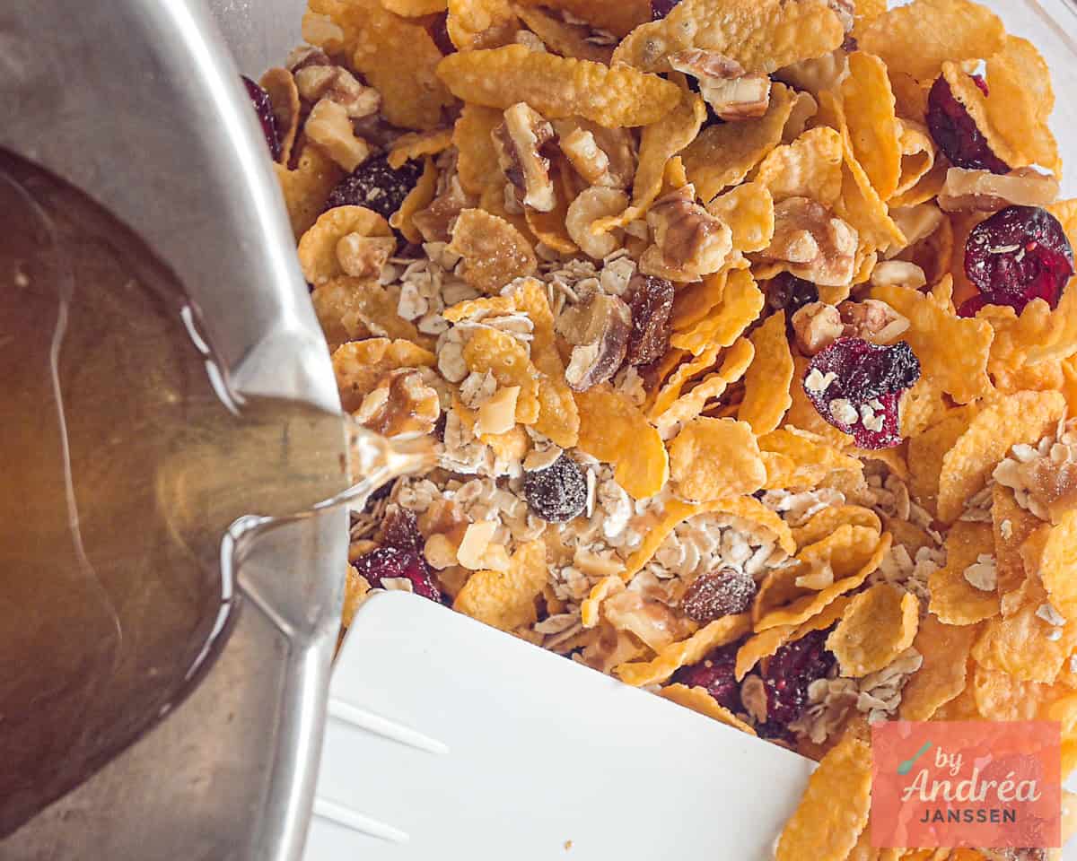 Warm honey is added to a bowl with cornflakes, oats, dried fruits and walnuts