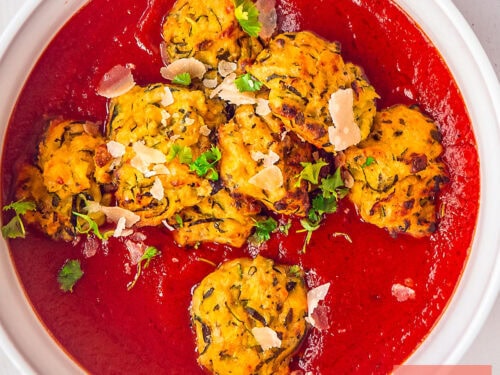 A square photo of a white bowl with tomato sauce and zucchini meatballs, delicious vegetarian.