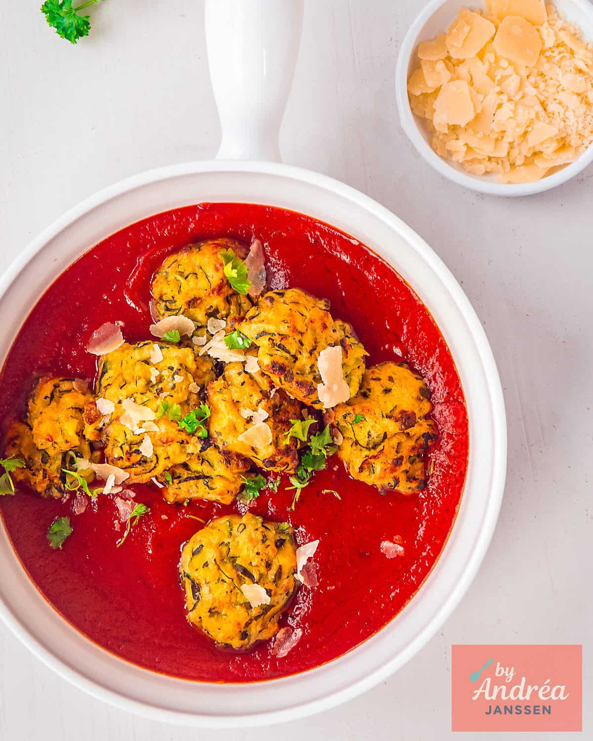 Een witte schaal met vegetarische courgette gehaktballetjes in tomatensaus en Parmezaanse kaas in de bovenhoek.