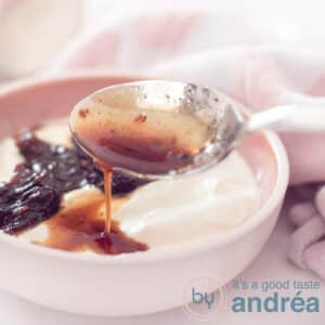 A square photo with part of a pink dish with soaked plum compote on Greek yogurt. A pink and white checkered tea towel lies diagonally above it.