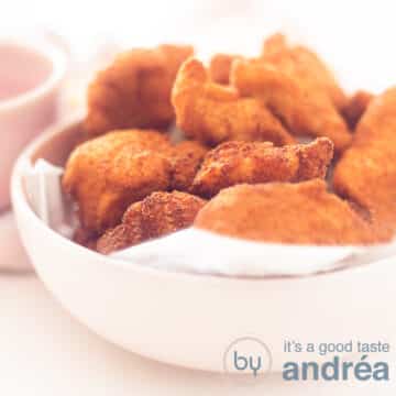 A square photo with a pink bowl filled with chicken nuggets. A white background.