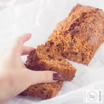 A square photo of part of a carrot cake with two slices cut off. A hand grabs the top slice.