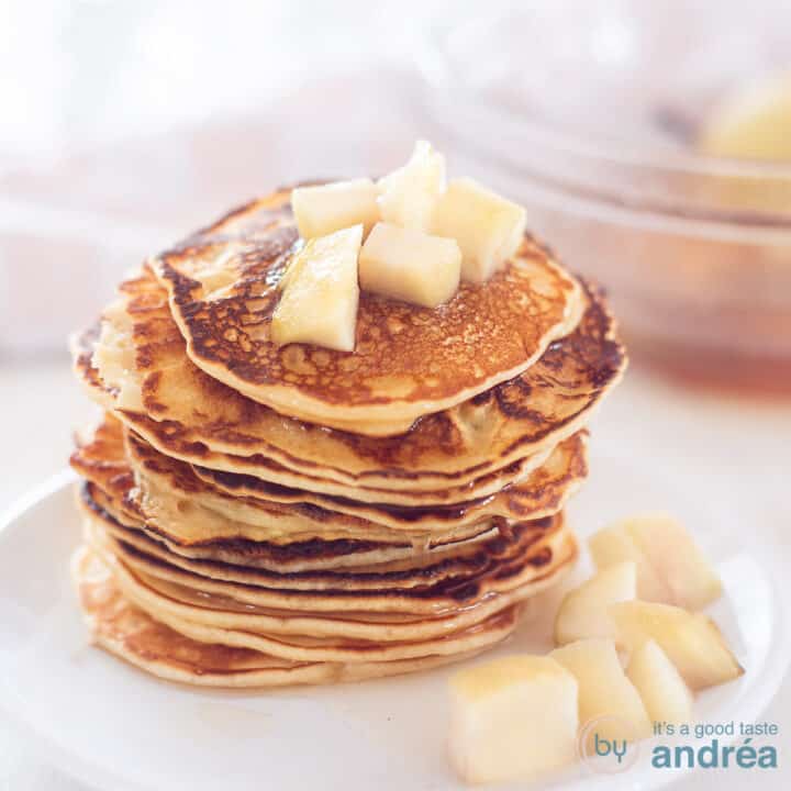 A square photo with a white plate with a stack of pancakes and stewed pears on top and around it.