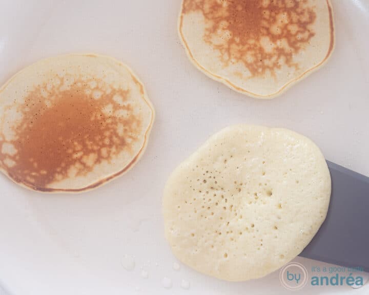 A white frying pan with three pancakes. Two already turned over, one is just being turned over