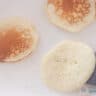 A white frying pan with three pancakes. Two already turned over, one is just being turned over